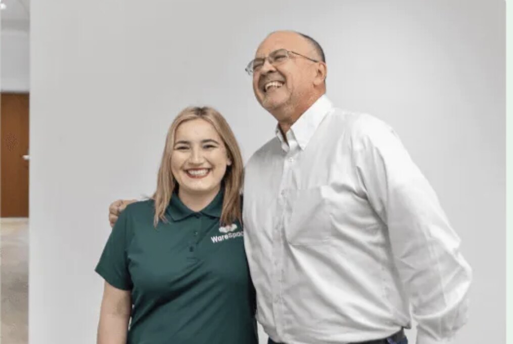 A WareSpace on-site General Manager in a green polo smiling alongside a happy tenant inside a building
