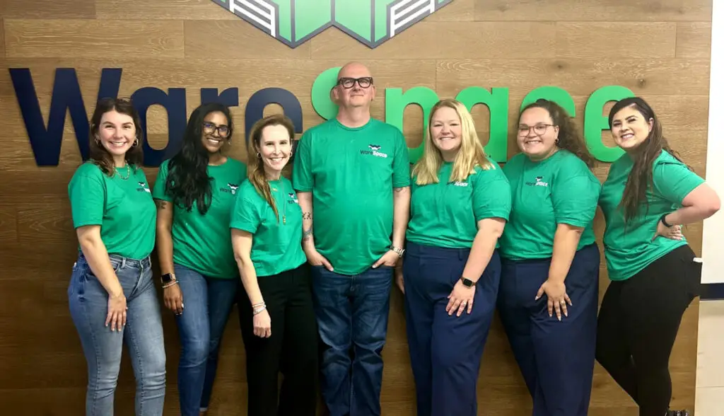 WareSpace staff group photo in front of a wooden wall with the company logo. The team is wearing matching green T-shirts.